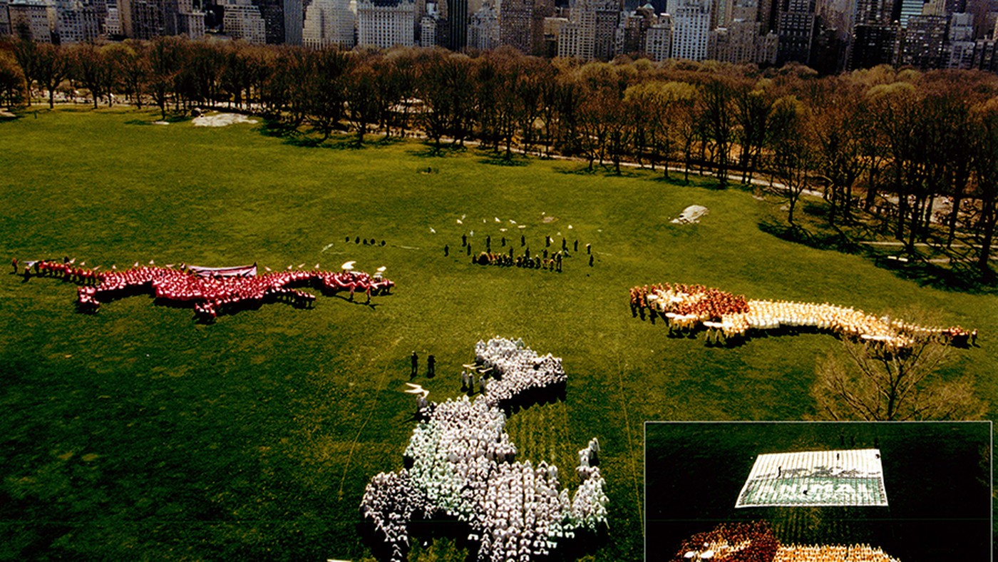 Thousands of people arranged into giant animal shapes on the Great Lawn in Central Park, with the Manhattan skyline behind